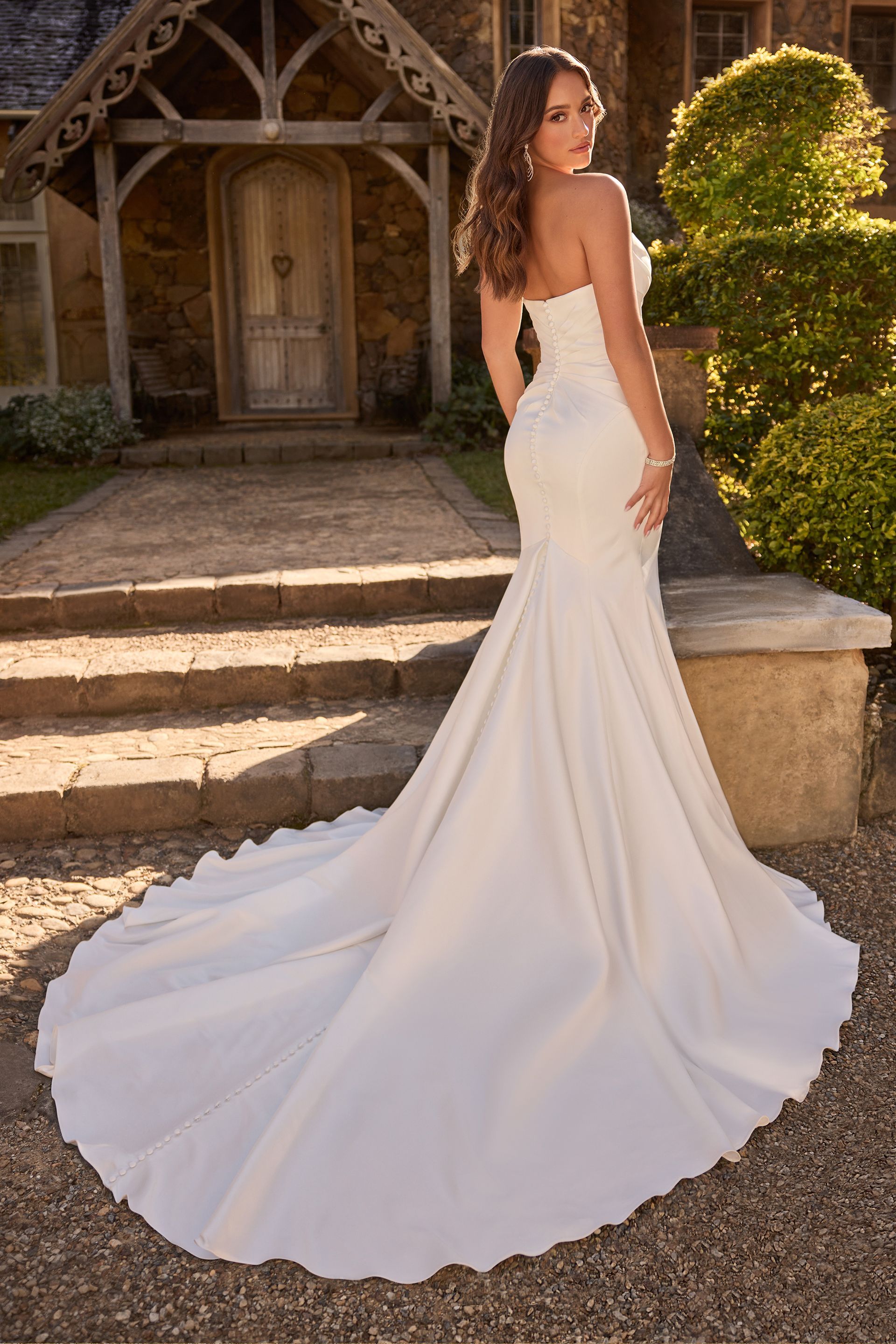 Woman in strapless white wedding dress with a train, outdoors.