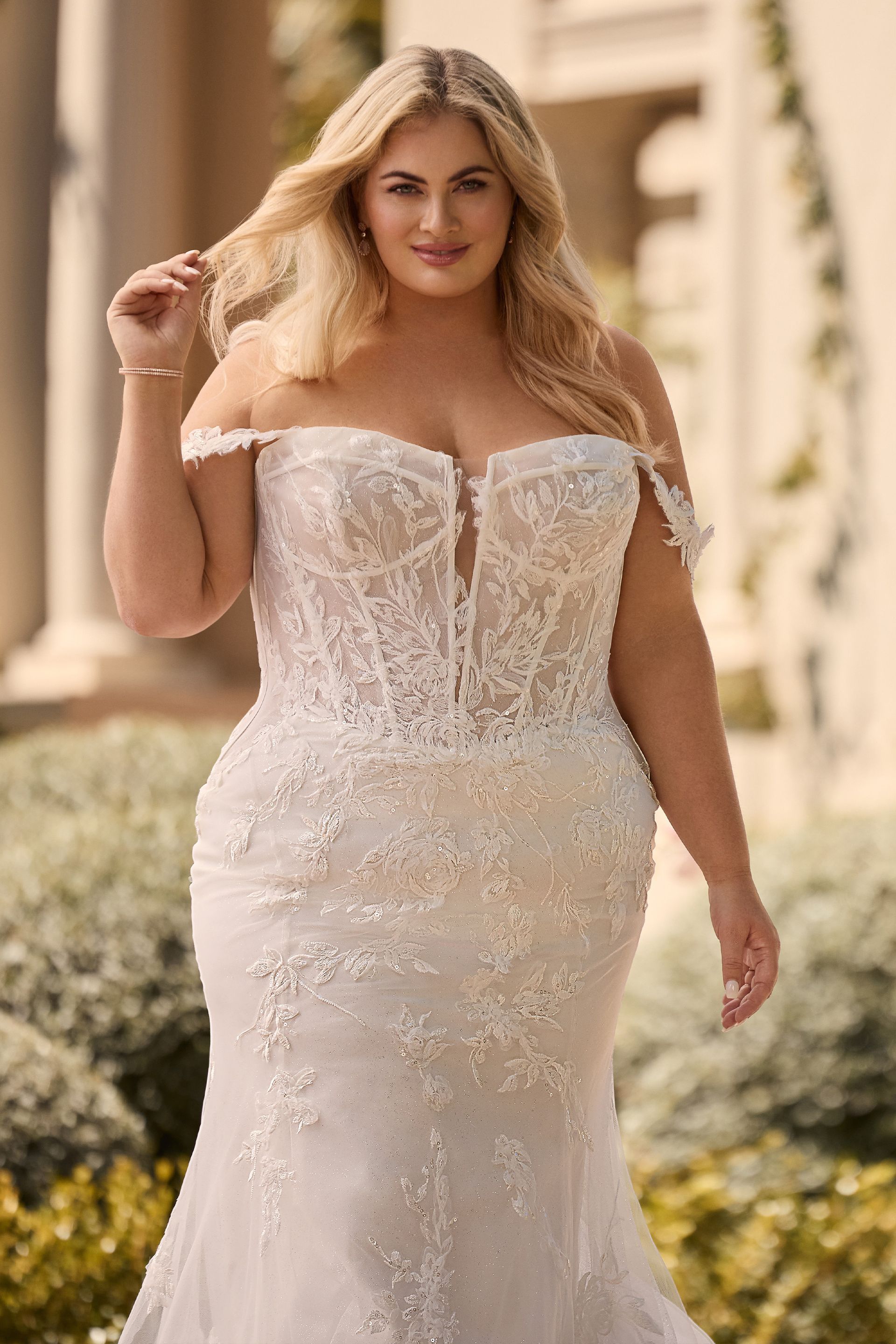 Woman in a white, off-the-shoulder wedding gown, posing outdoors.