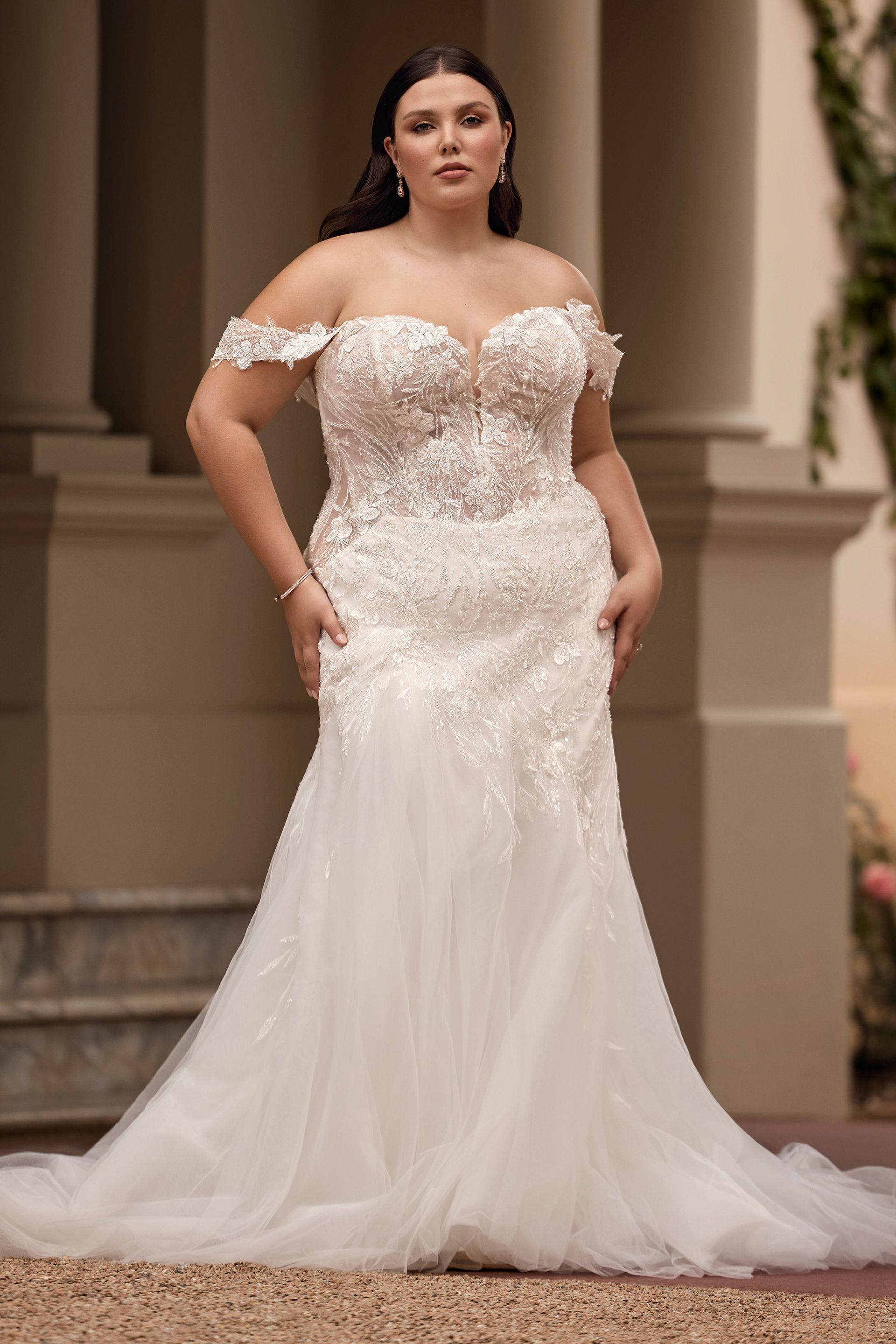 Woman in a white off-the-shoulder wedding dress, standing outdoors.