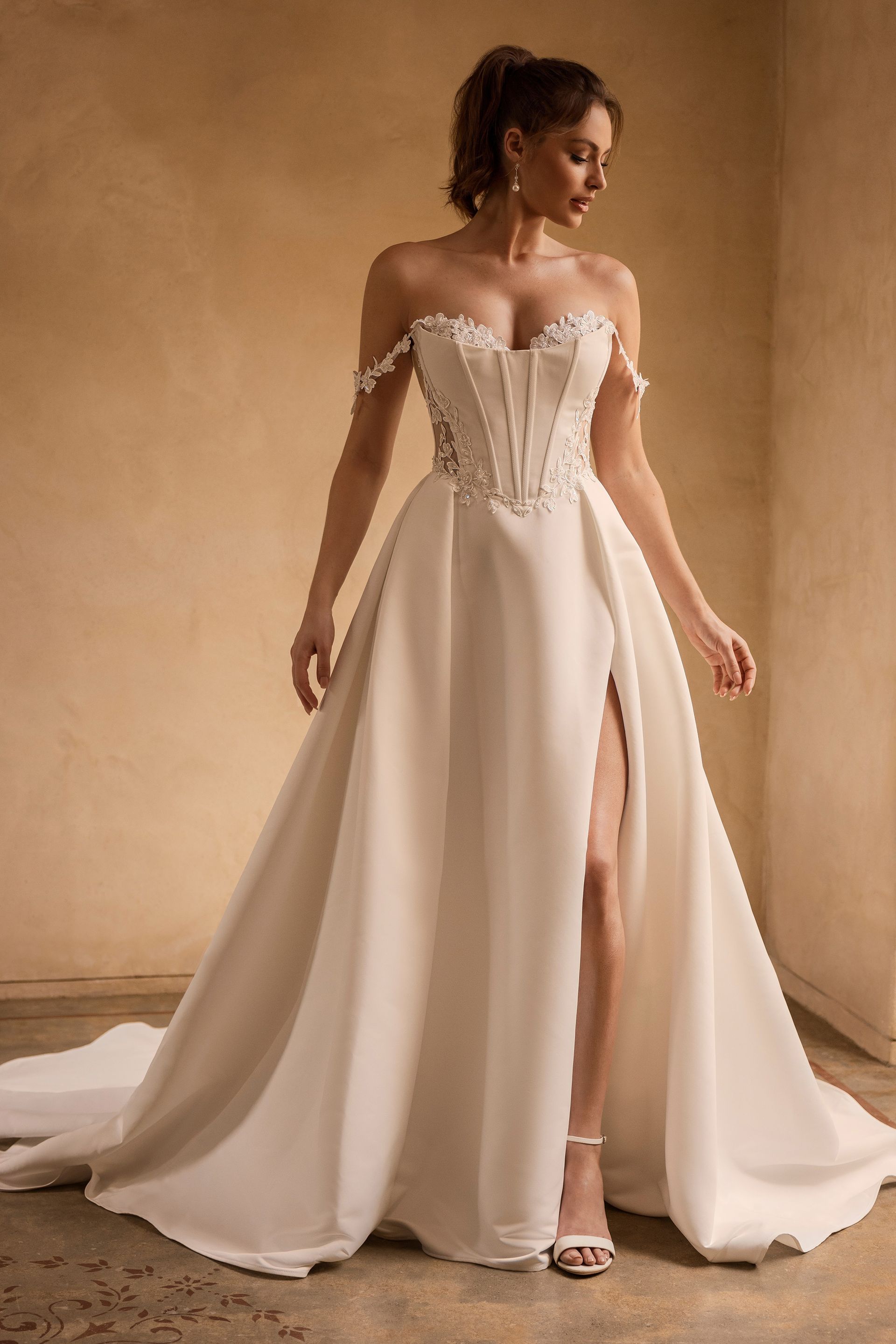 Woman in strapless white wedding dress with high slit, standing in a studio.
