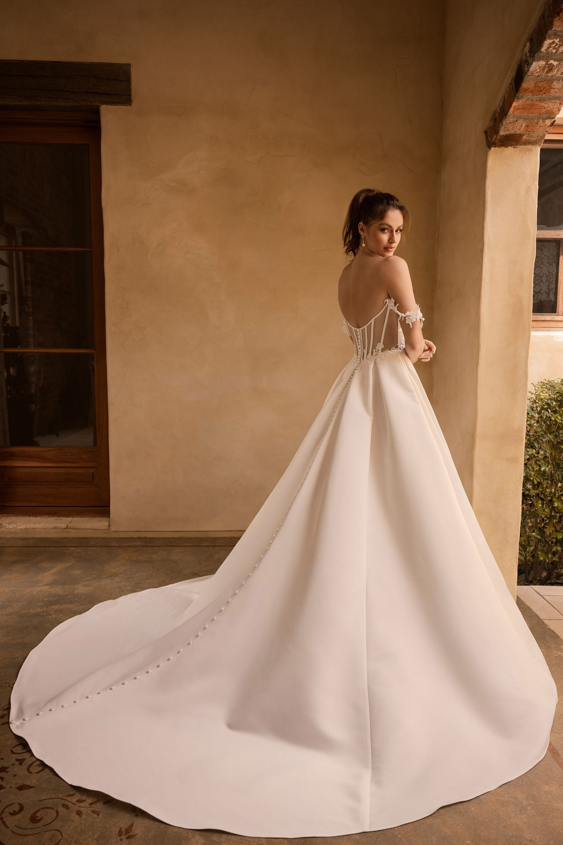 Woman in strapless white wedding dress with high slit, standing in a studio.
