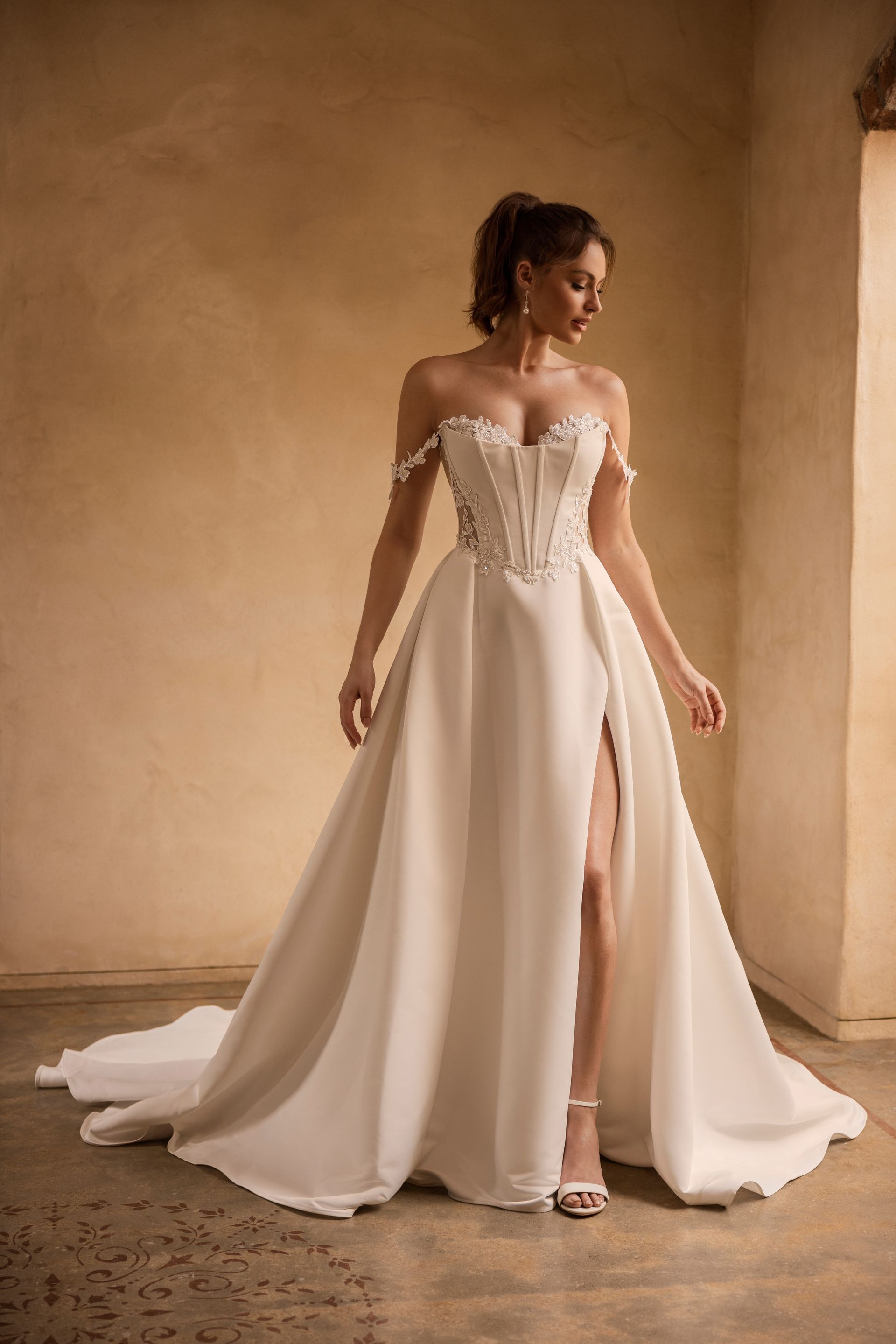 Woman in strapless white wedding dress with high slit, standing indoors.