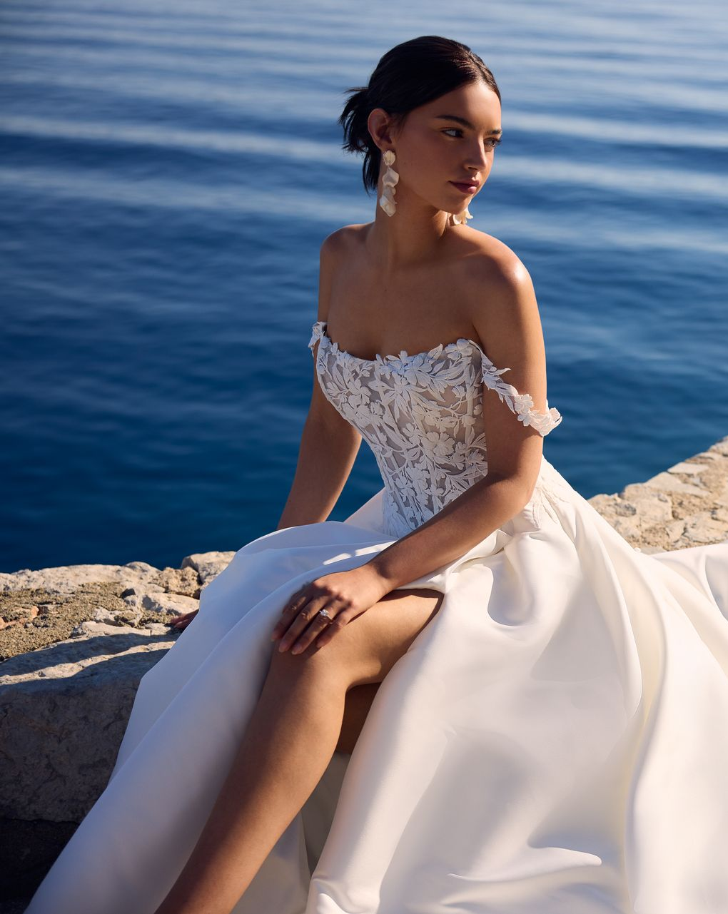 Woman in a cream strapless gown standing by a stone arch with a seaside view behind her