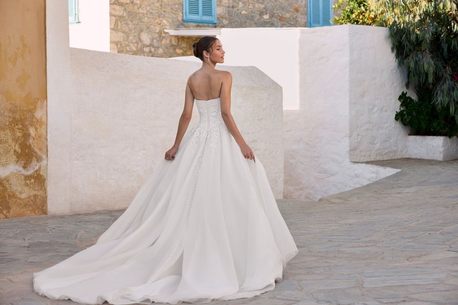 Woman in a white off-the-shoulder wedding dress with a long veil, standing outdoors.