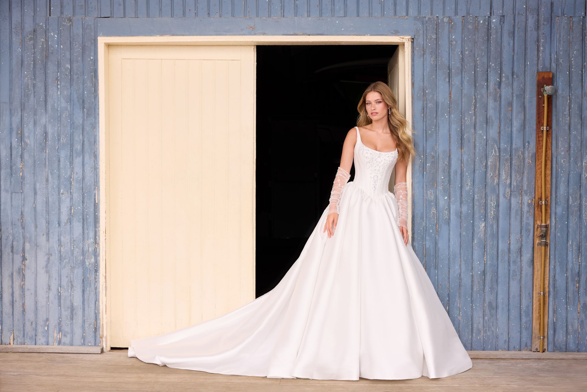 Woman in a white wedding dress seated by a window, looking to the side.