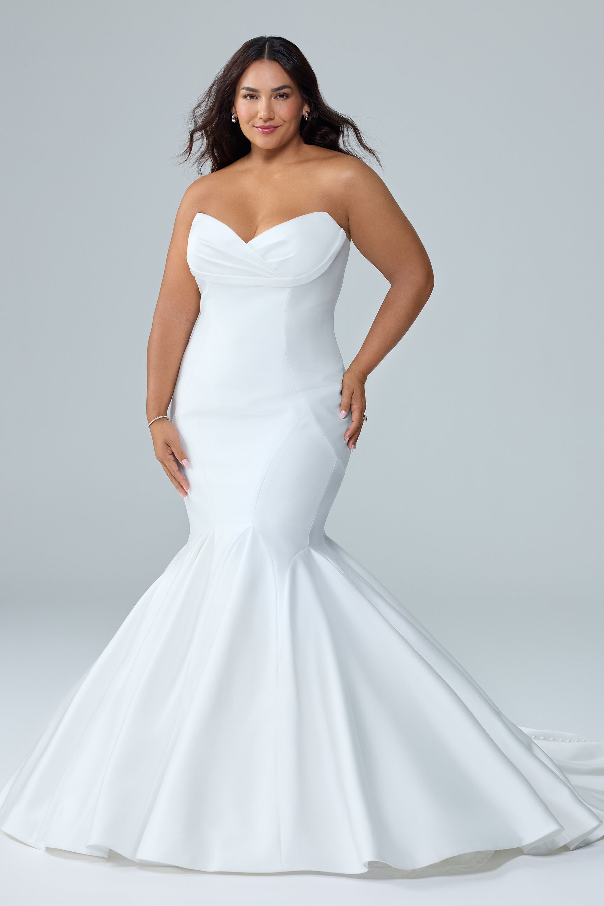 Woman in a strapless white mermaid wedding gown posing against a gray studio backdrop Woman in a strapless white mermaid wedding gown posing against a gray studio backdrop