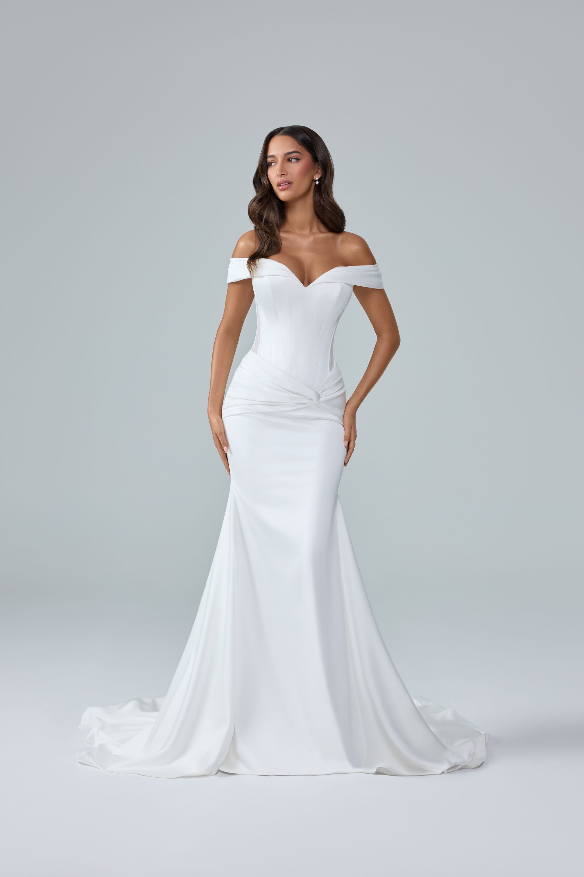 Woman in a white strapless wedding gown with a long train, standing against a gray studio backdrop Woman in a white strapless wedding gown with a long train, standing against a gray studio backdrop