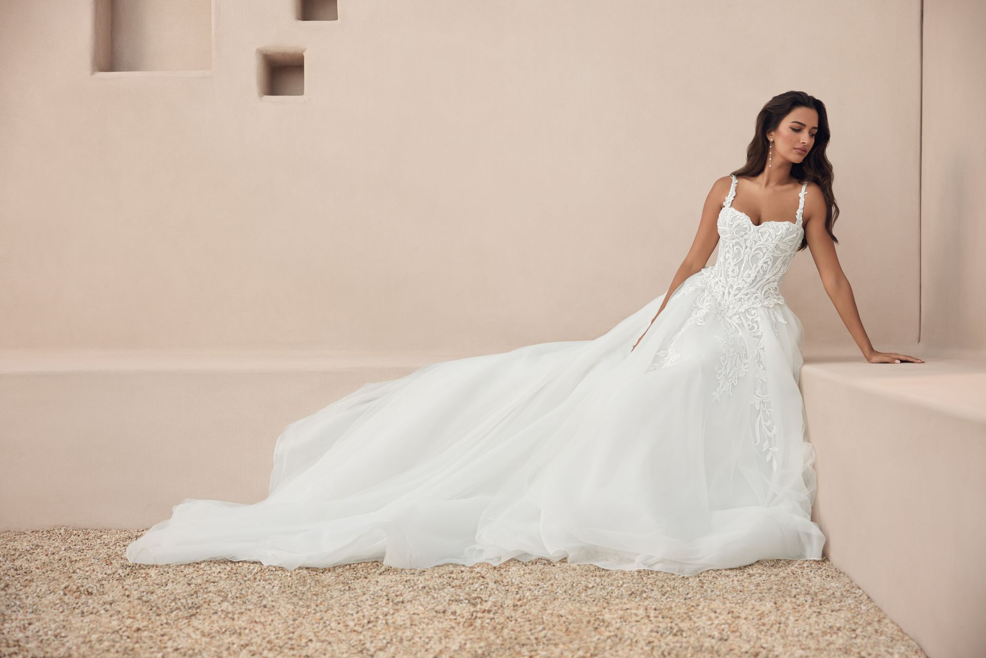 Woman in a white wedding gown leaning against a beige wall in a minimalist studio setting Woman in a white wedding gown leaning against a beige wall in a minimalist studio setting