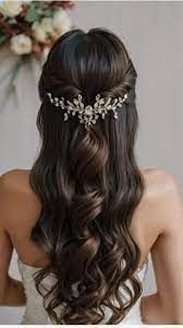 Woman with dark wavy hair, half up, adorned with a jeweled hairpiece, wearing a white strapless dress.