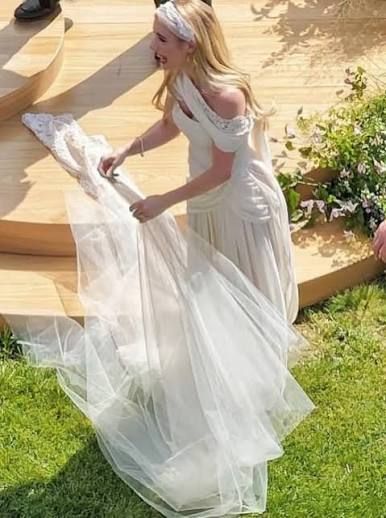 Blonde woman in a white dress holding a long flowing train on sunlit garden steps