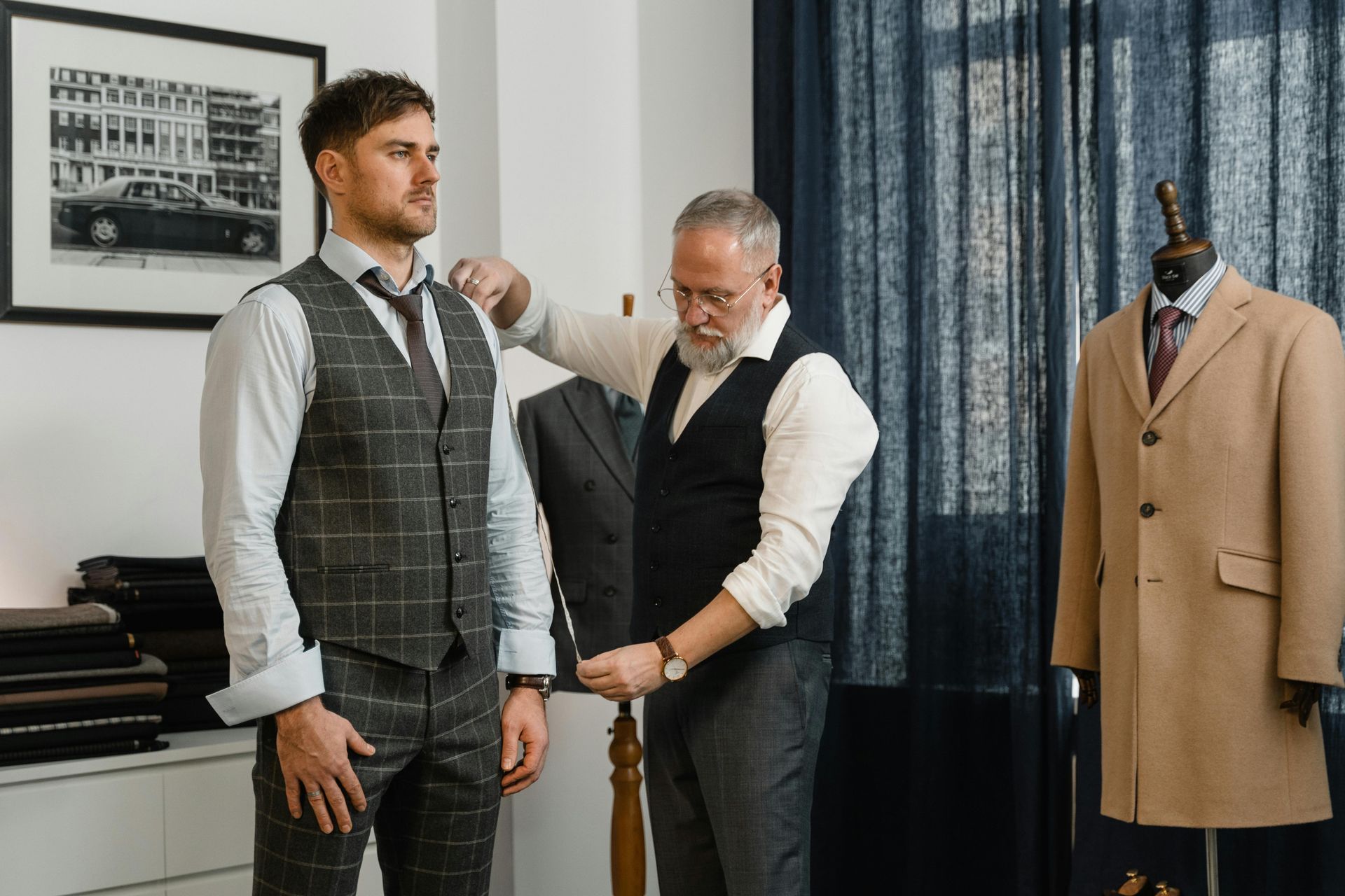 Tailor measuring a customer wearing a checkered vest in a menswear shop.