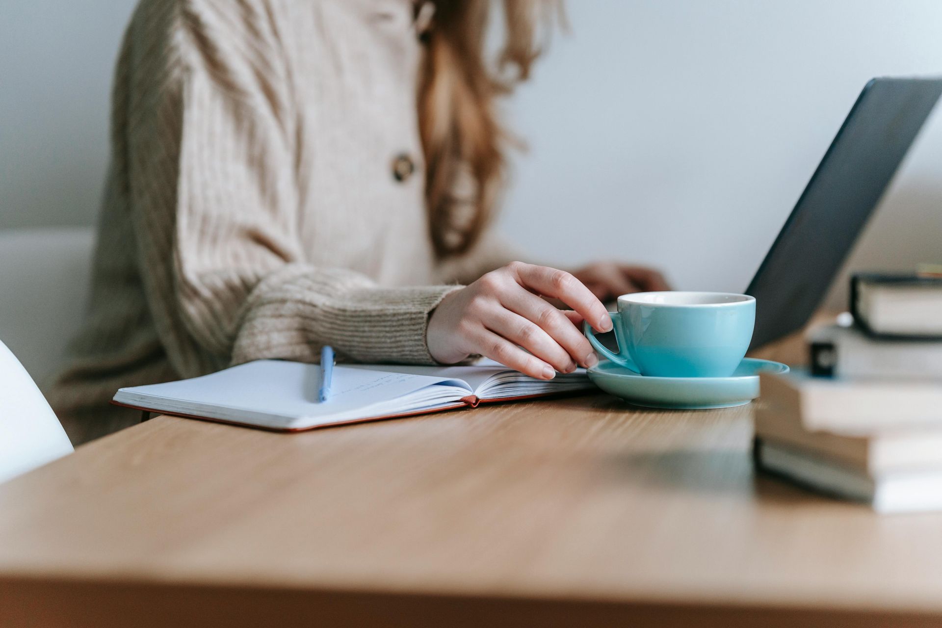 Person seated at a desk, typing on a laptop, with a coffee cup and notebook.