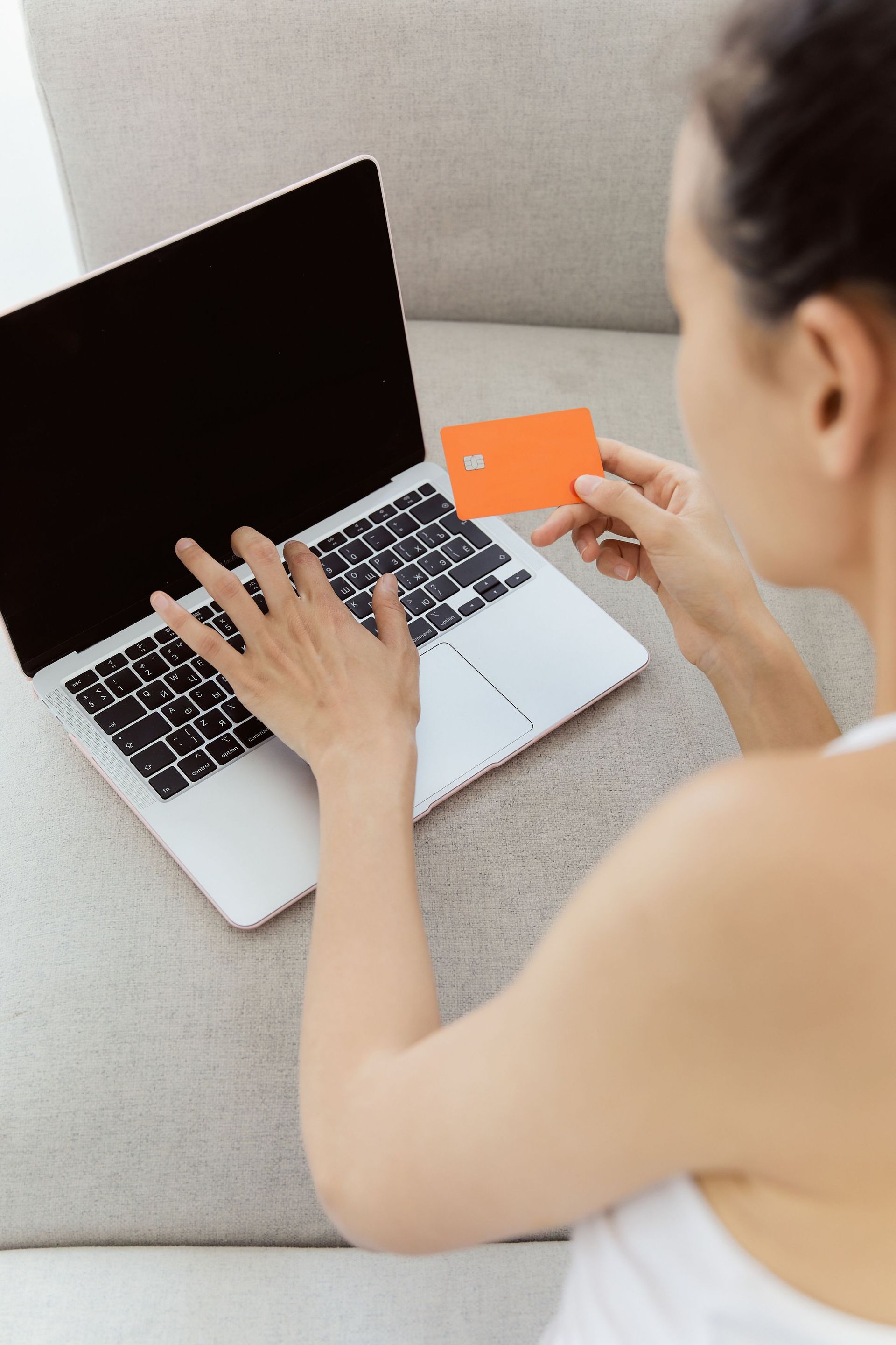 Person using a laptop and holding an orange card on a couch Person using a laptop and holding an orange card on a couch