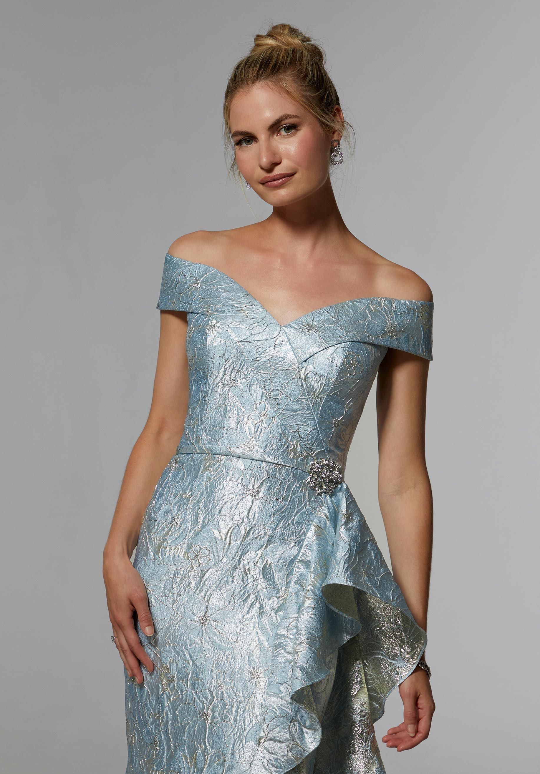 Woman in a light blue off-the-shoulder gown with ruffled side detail poses in a studio.