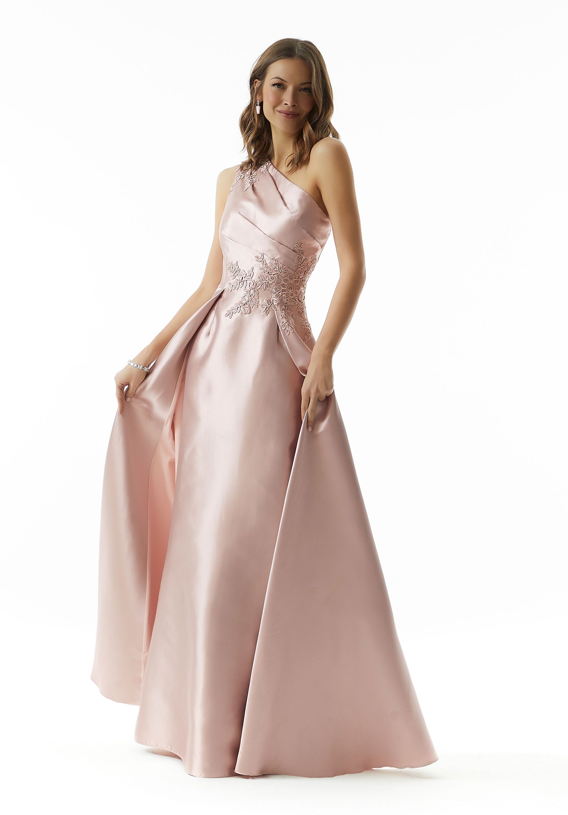 Woman in a light pink one-shoulder gown, posing with dress held out.