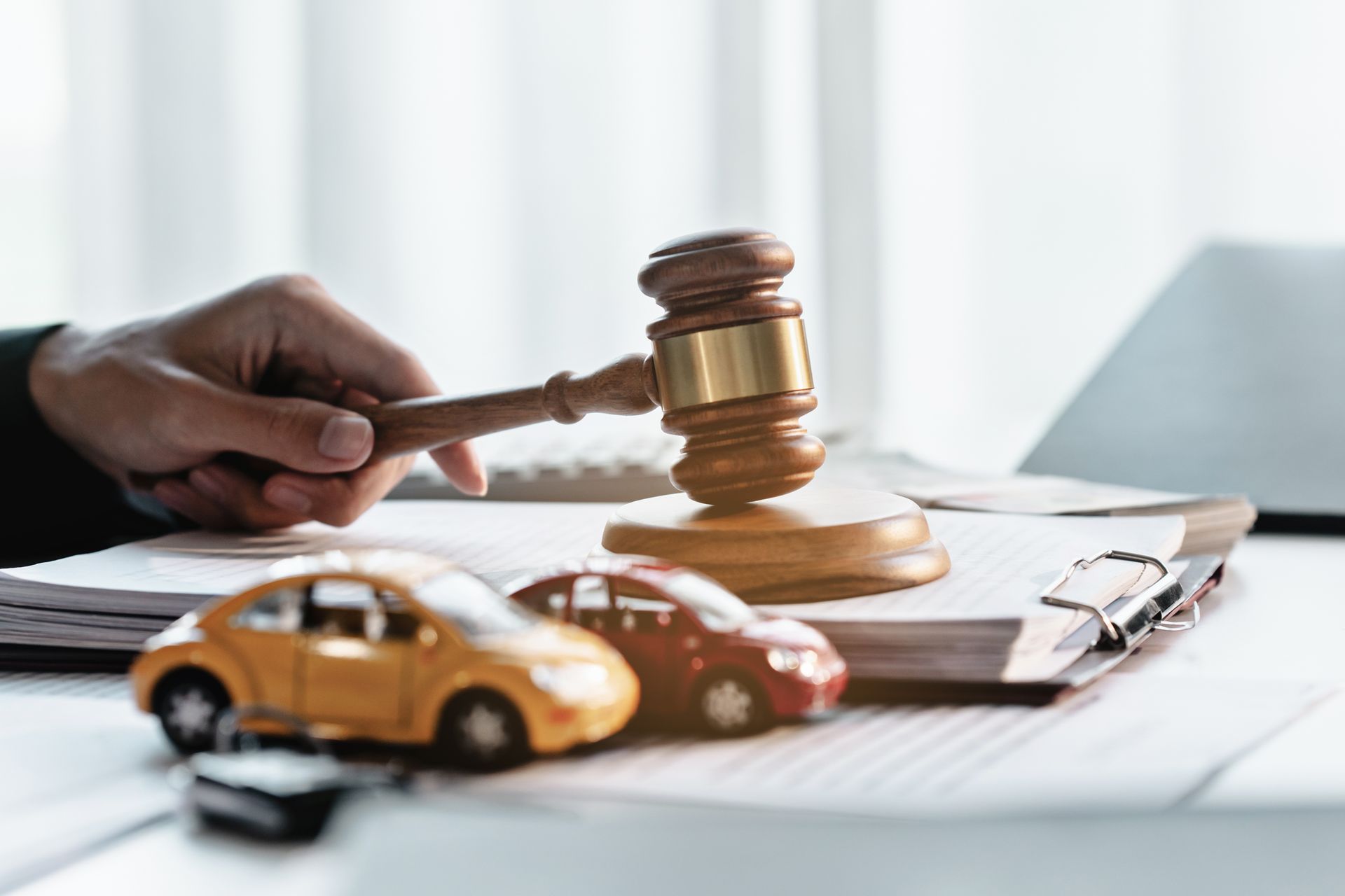 Hand holding gavel above papers beside a toy car, symbolizing a legal case or insurance claim