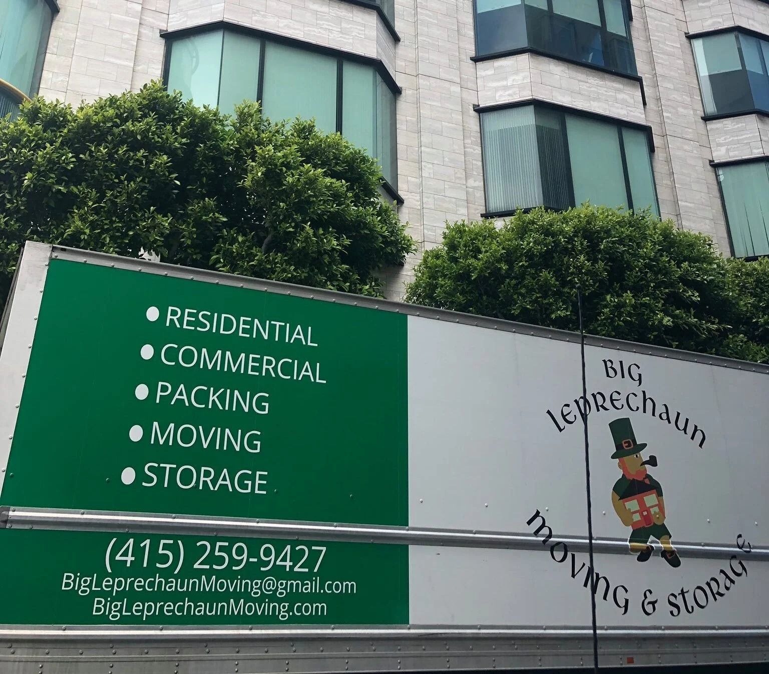 A moving truck side featuring a green panel with list of services, phone number, and a logo of a leprechaun.