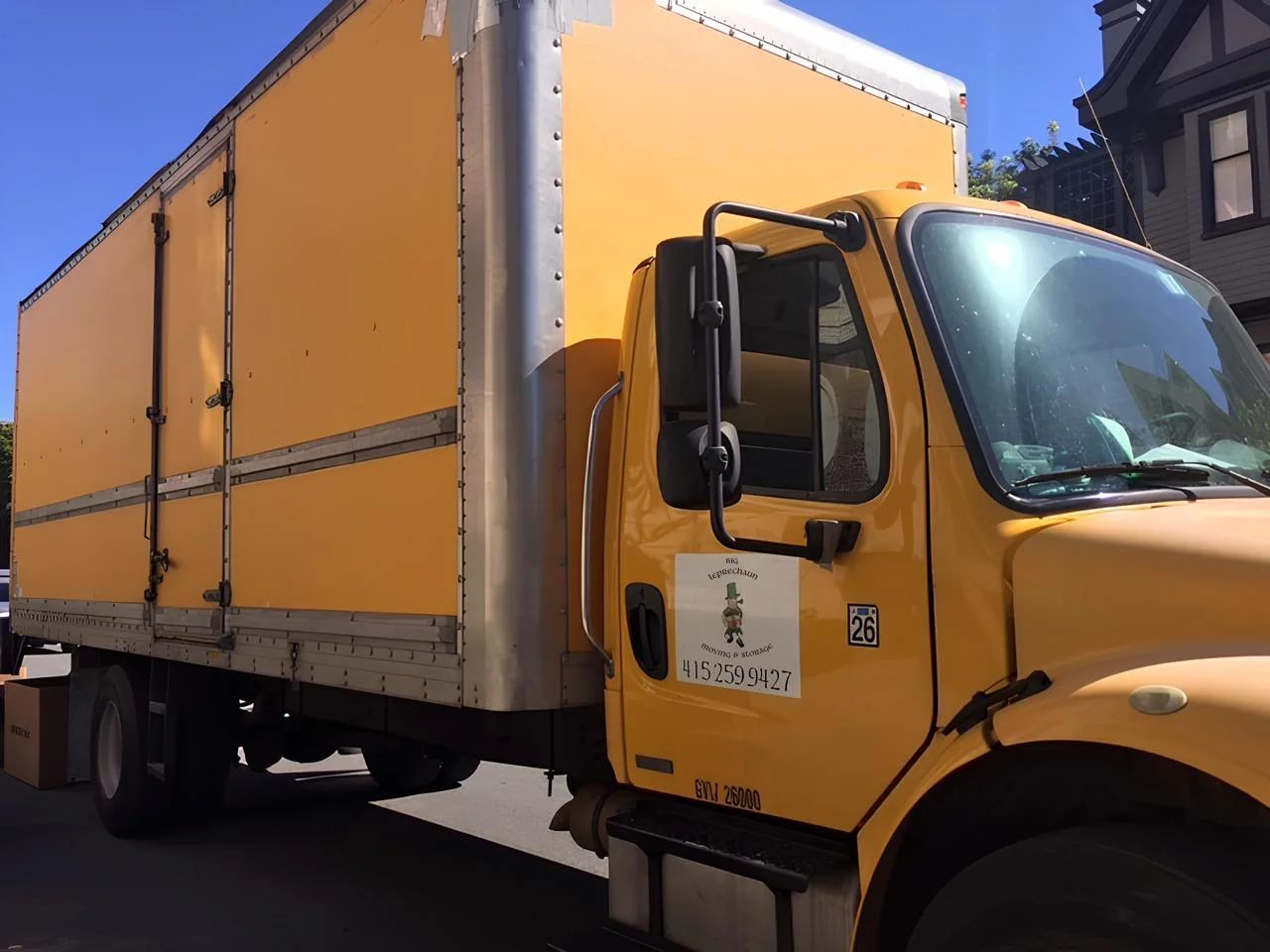 A yellow box truck parked on a street in front of a house.