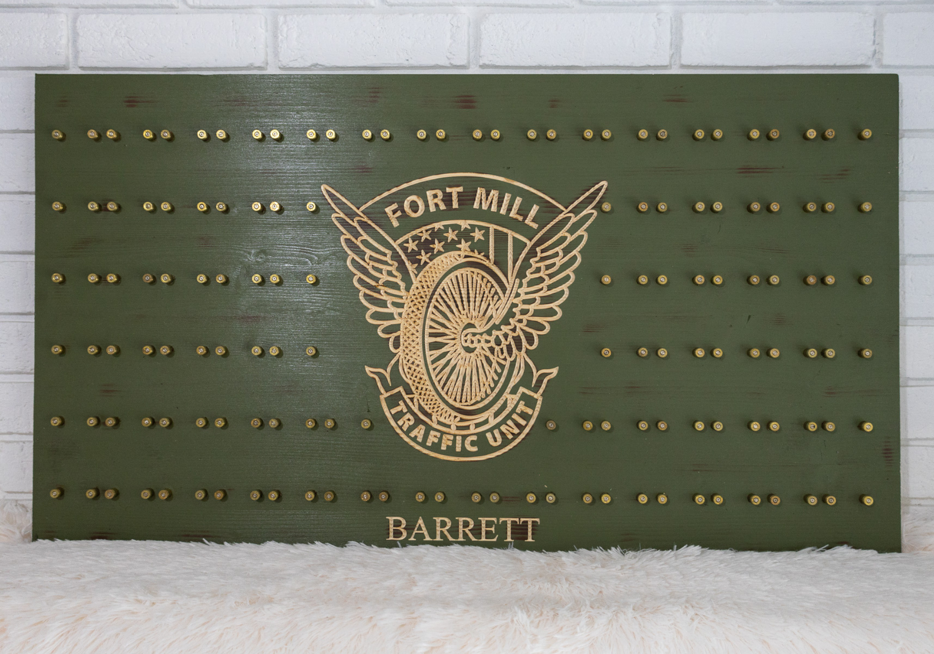 Green wooden plaque with a Fort Mill Traffic Unit logo and small brass pegs, displayed on a white surface.
