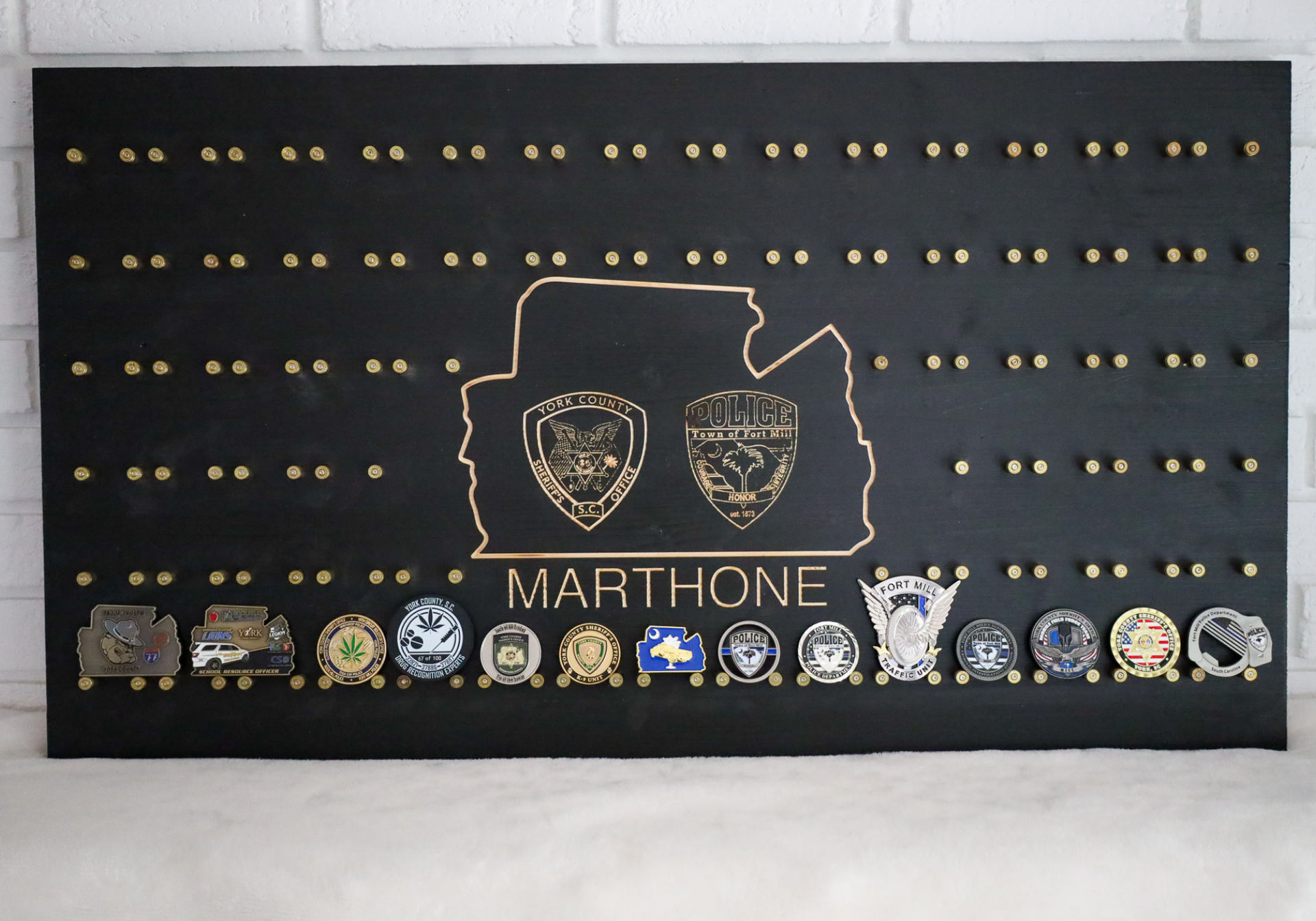 Black display board with gold pins holding challenge coins; a gold emblem says 