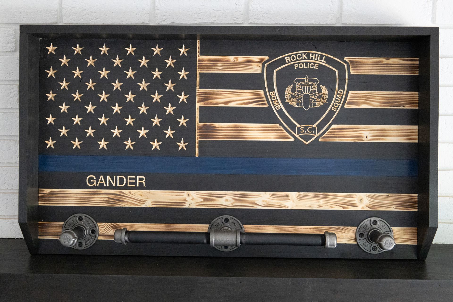 Wooden American flag plaque with police badge emblem and four hooks, labeled “GANDER.”