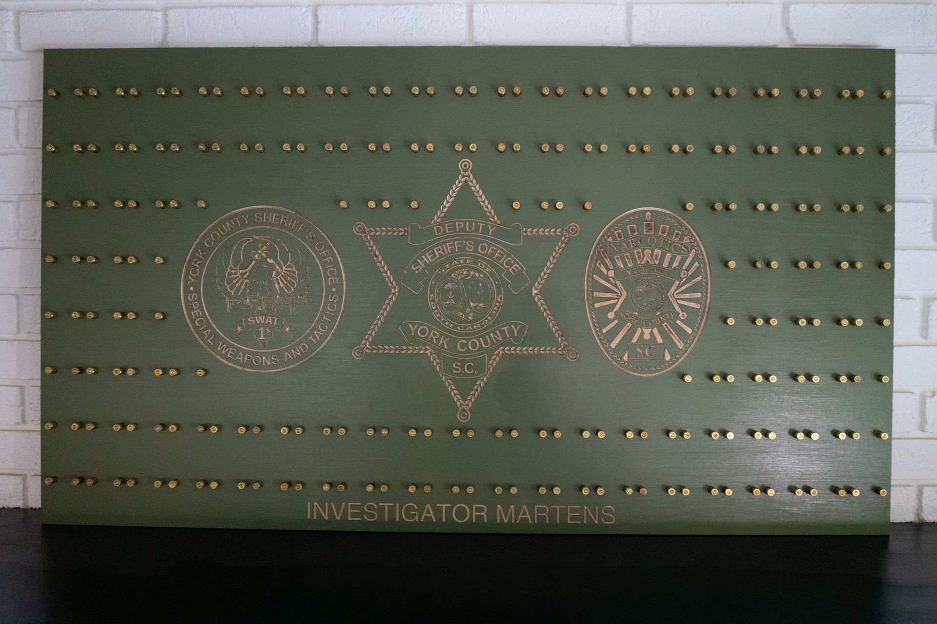 Green rectangular board with gold dots and three starburst emblems on a tiled wall
