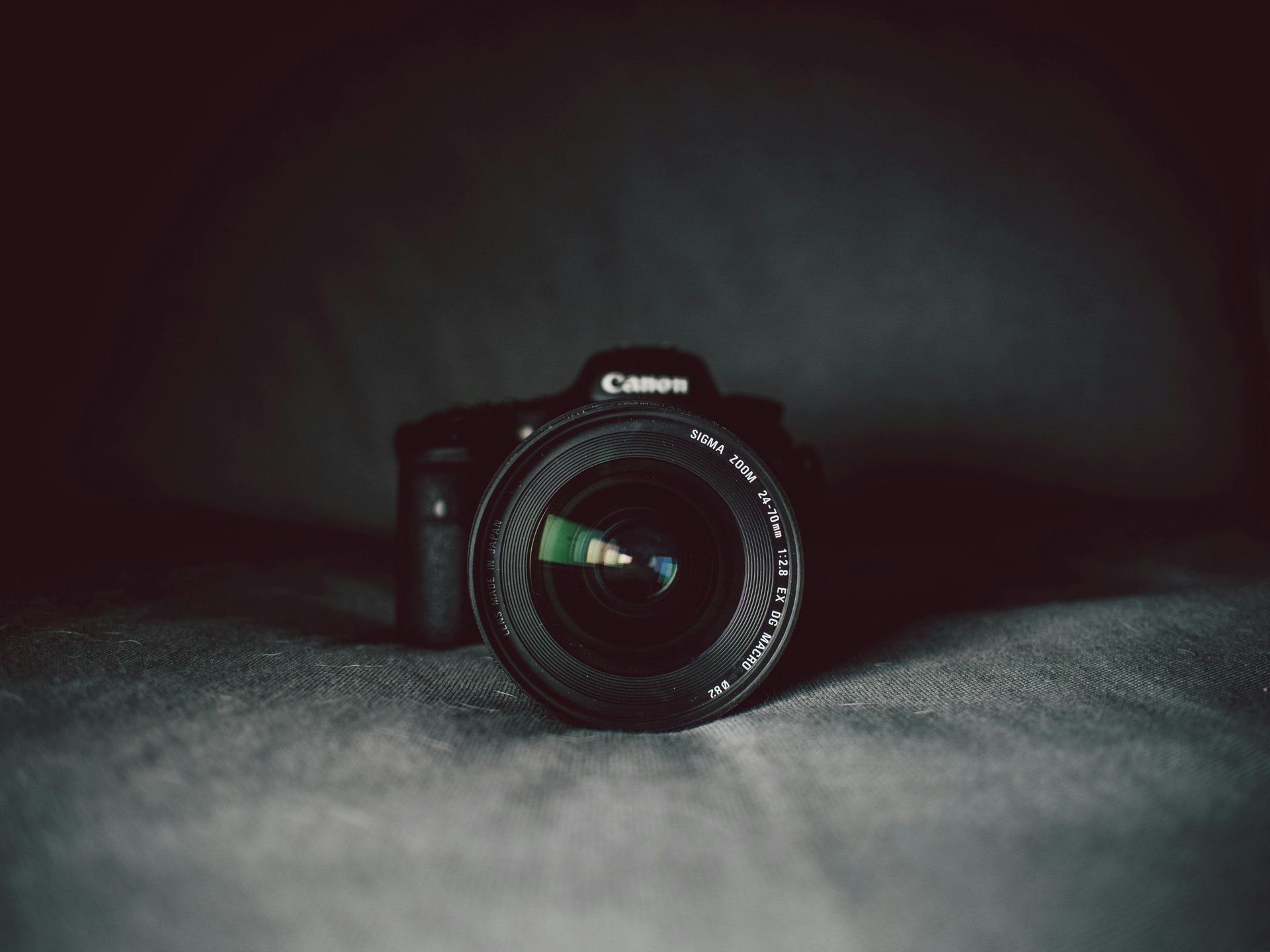 Canon camera with lens facing forward, sitting on textured gray surface, dark setting.