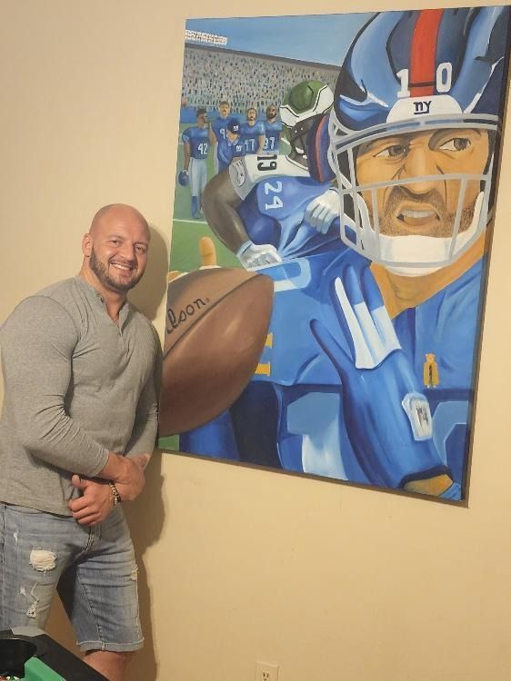 A man stands in front of a painting of a football player with the number 10 on his helmet