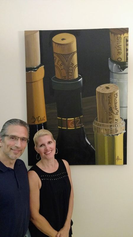 A man and a woman are standing in front of a painting of wine corks