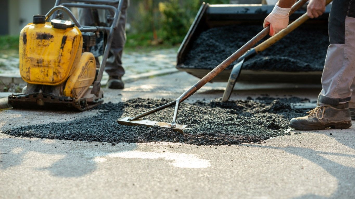 Workers leveling fresh asphalt with a rake and vibrating compactor on a road surface