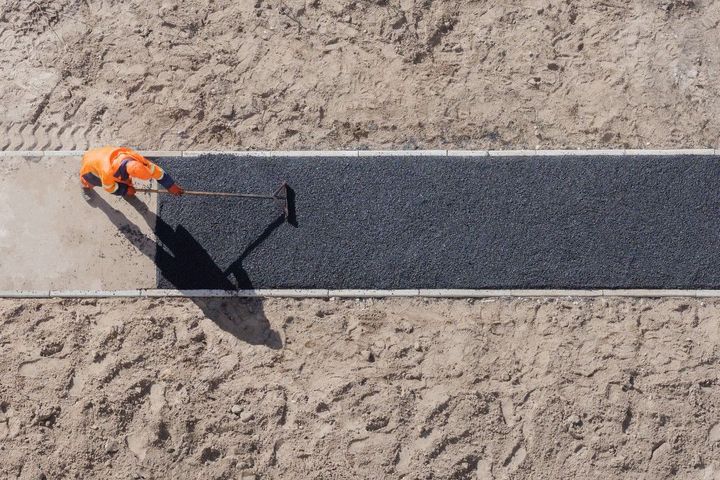 Construction worker spreading asphalt on a road with a rake from an overhead view