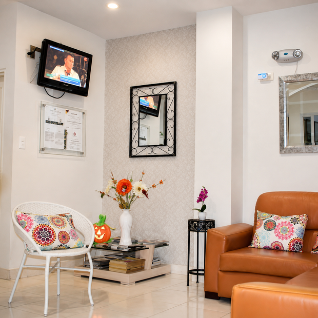 Sala de estar moderna con sofá naranja, silla blanca, televisor montado en la pared, espejo y decoración floral.