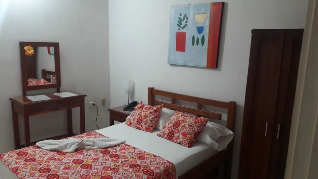 Dormitorio con cama de madera, ropa de cama con estampado rojo, tocador, armario y arte abstracto en la pared.