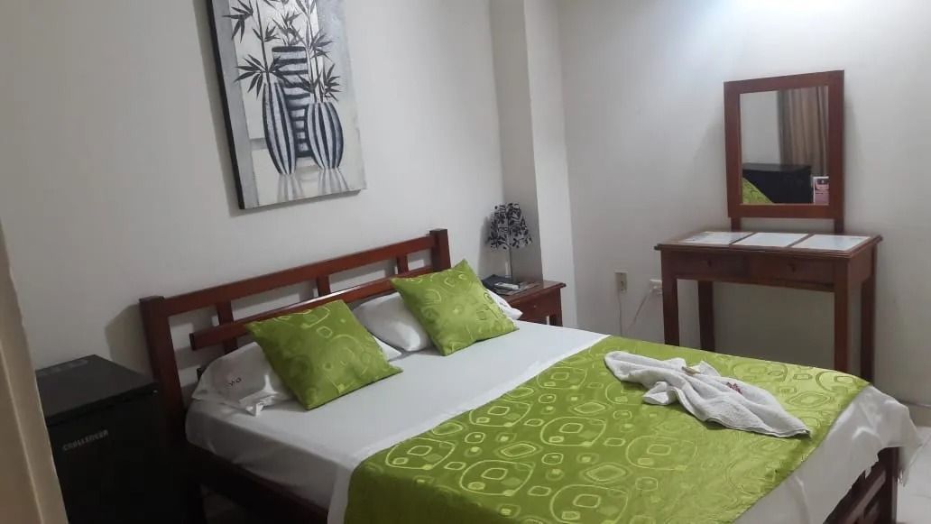 Dormitorio con cama de madera, ropa de cama y almohadas verdes