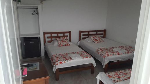 Habitación pequeña con tres camas individuales, paredes blancas y un armario en la esquina.
