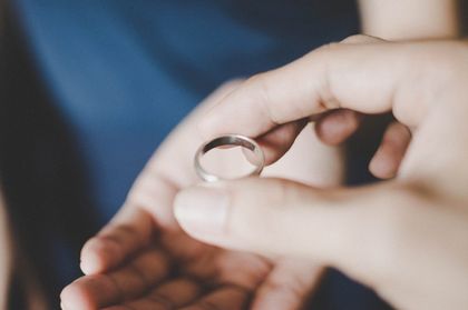 Hand holding a silver ring, offering it to another person, suggesting a proposal or removal.