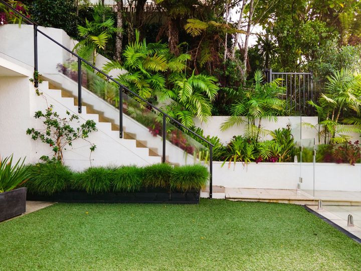 Lush garden patio with green lawn, white stairs, and dense tropical plants along a wall