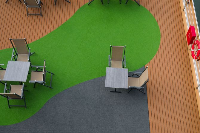 Overhead view of a patio with green turf, gray seating, and wood decking with orange chairs along the wall