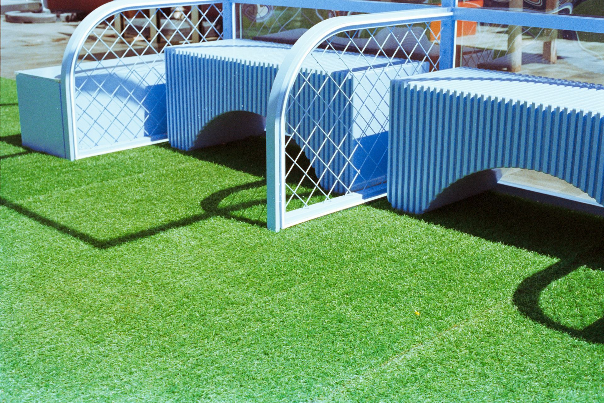 Blue-and-white outdoor benches on bright green grass, with curved white metal frames casting shadows