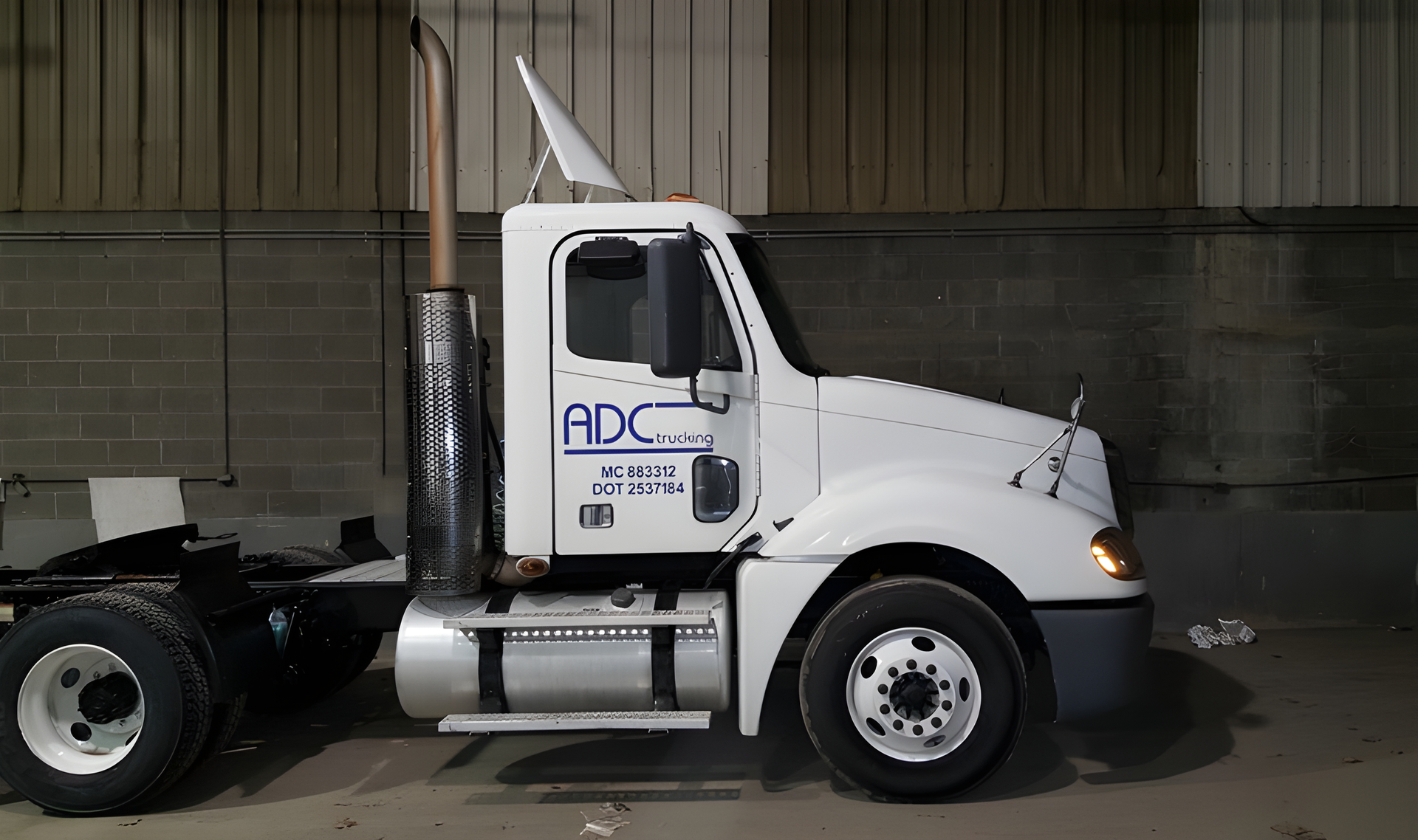 White semi truck cab parked indoors beside a gray cinderblock wall.