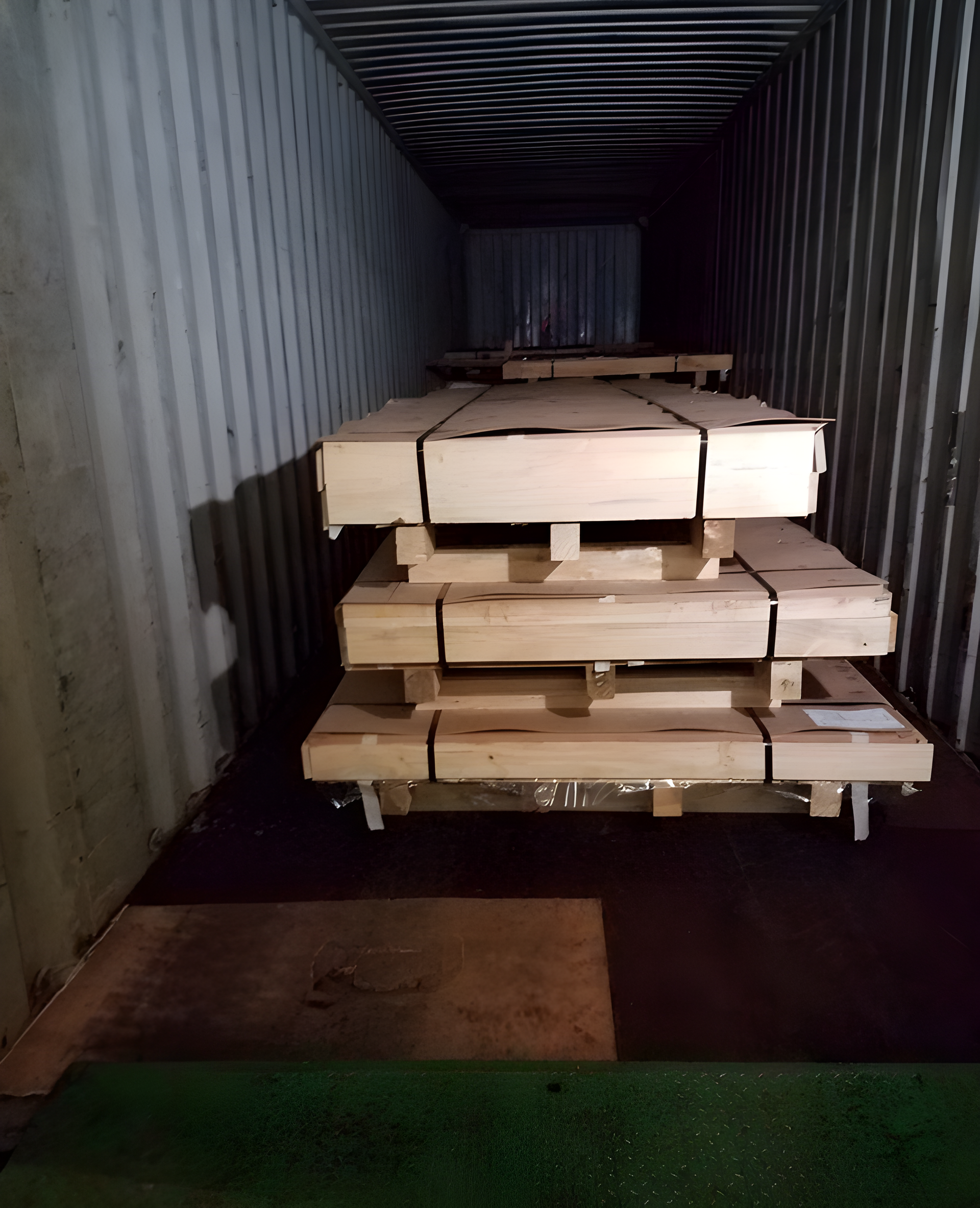 Stacked wooden boards/pallets inside a shipping container, viewed from the open end.