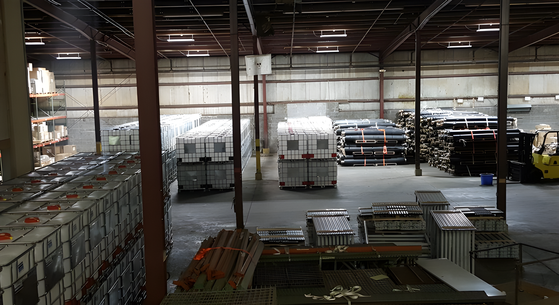 Large warehouse interior with stacks of pallets, metal racks, and industrial shelving under dim lighting