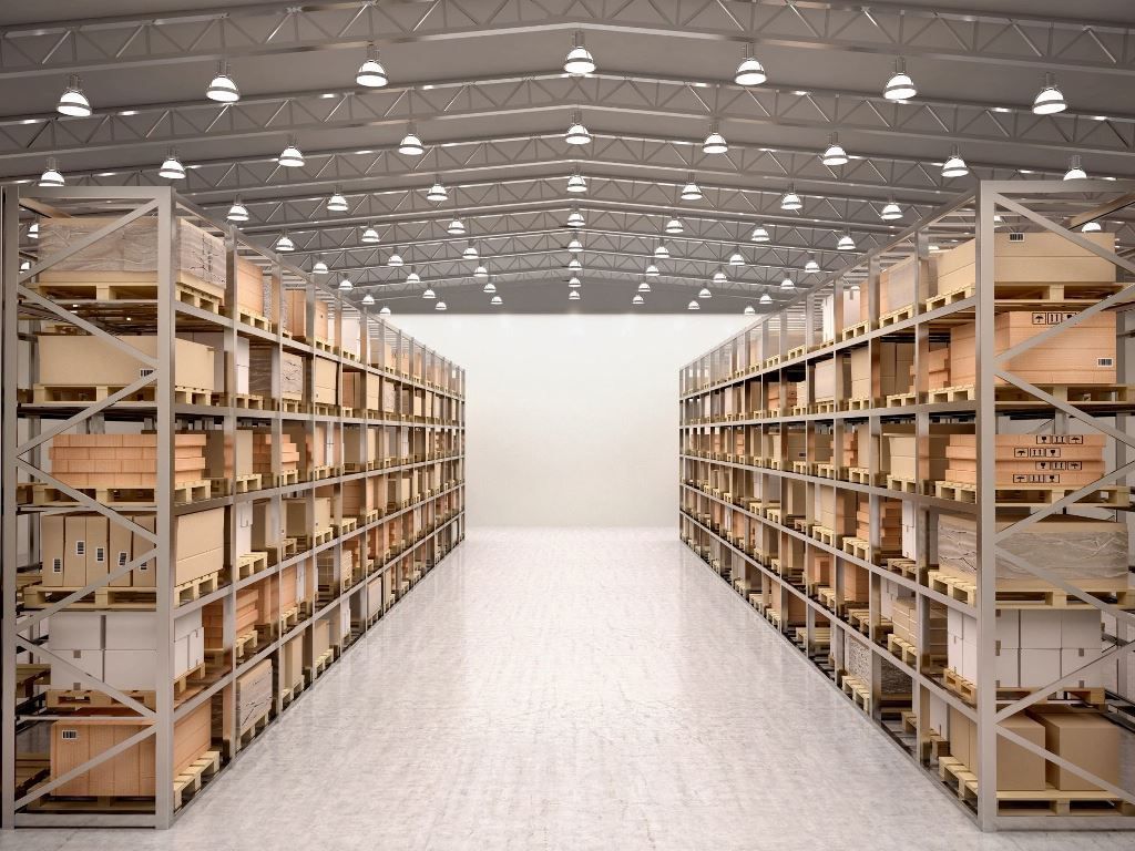 Aisle in a large warehouse with tall metal shelves stacked with cardboard boxes and supplies