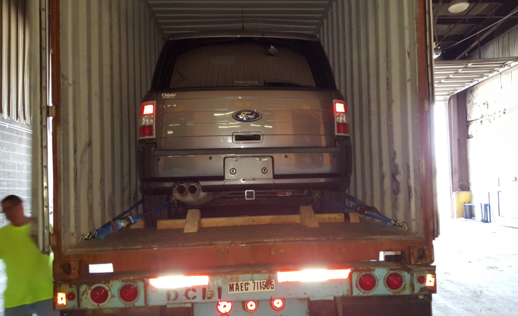 SUV strapped inside a shipping container on a flatbed truck, viewed from the rear