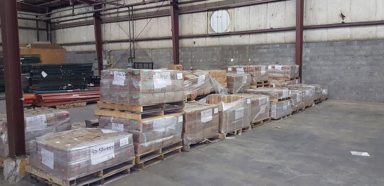 Warehouse aisle with stacked pallets of wrapped boxes and goods.