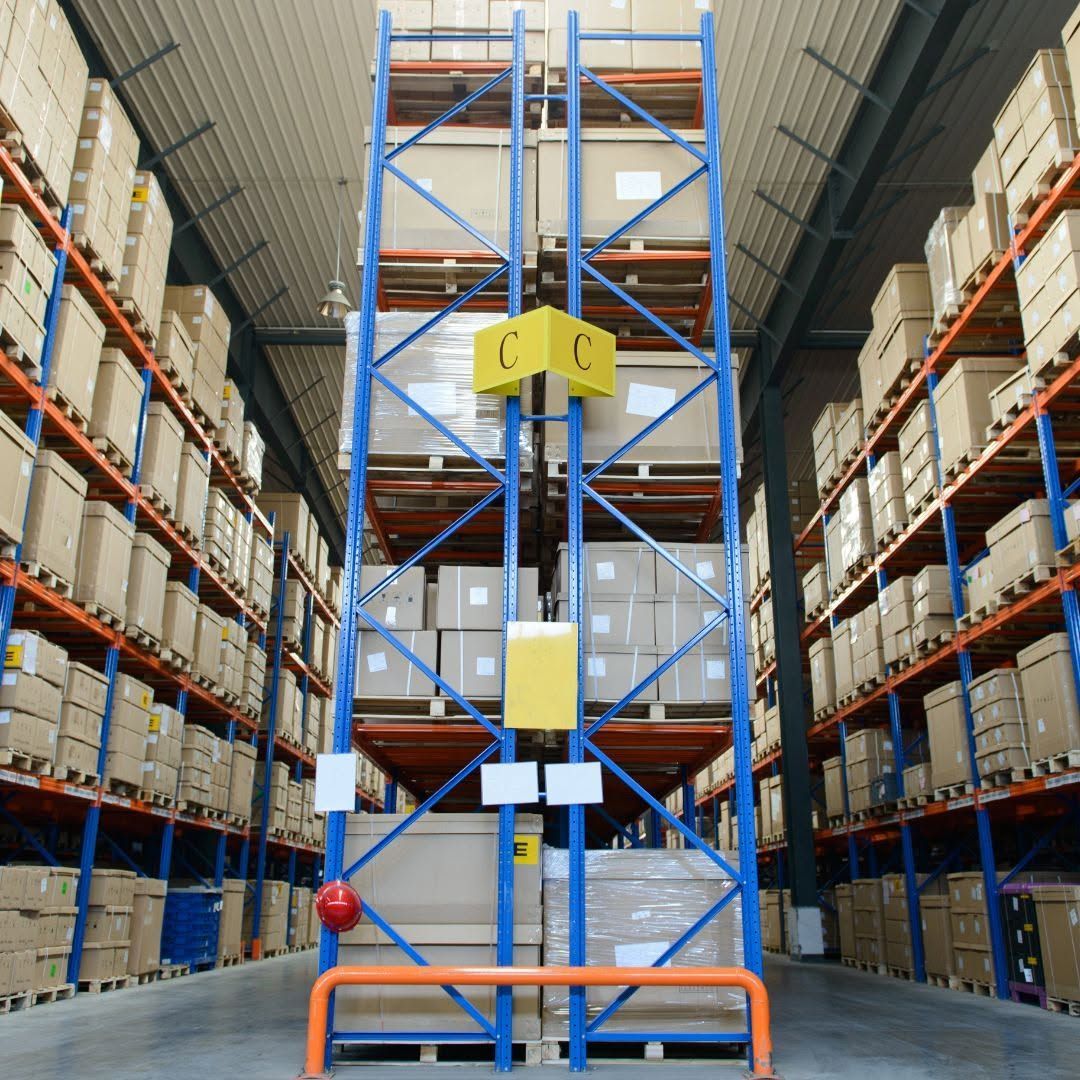 Warehouse aisle with tall pallet racks and a yellow-blue order picker in the center.