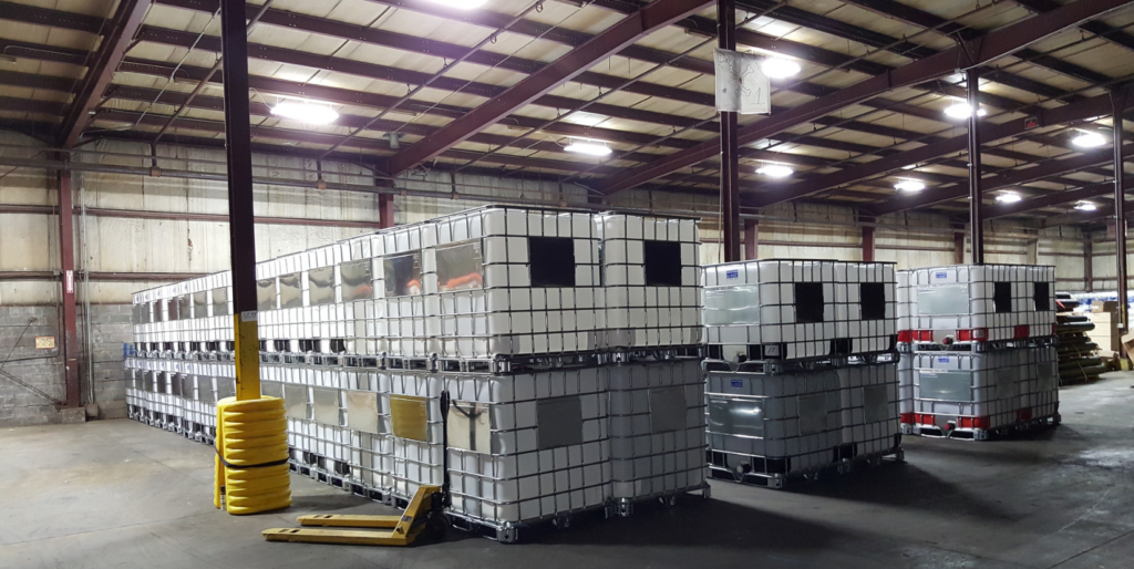 Warehouse interior with stacks of white palletized containers under metal beams and overhead lights