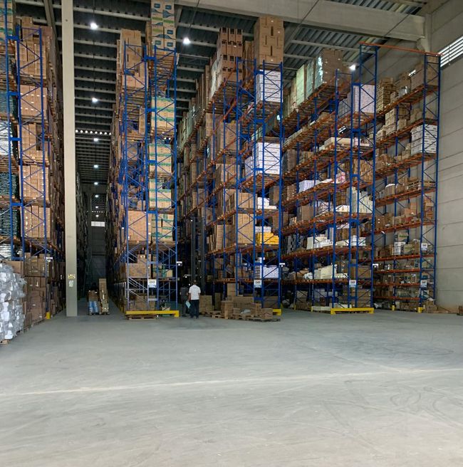 Large warehouse interior with tall blue shelving, stacked boxes, and two workers on a concrete floor