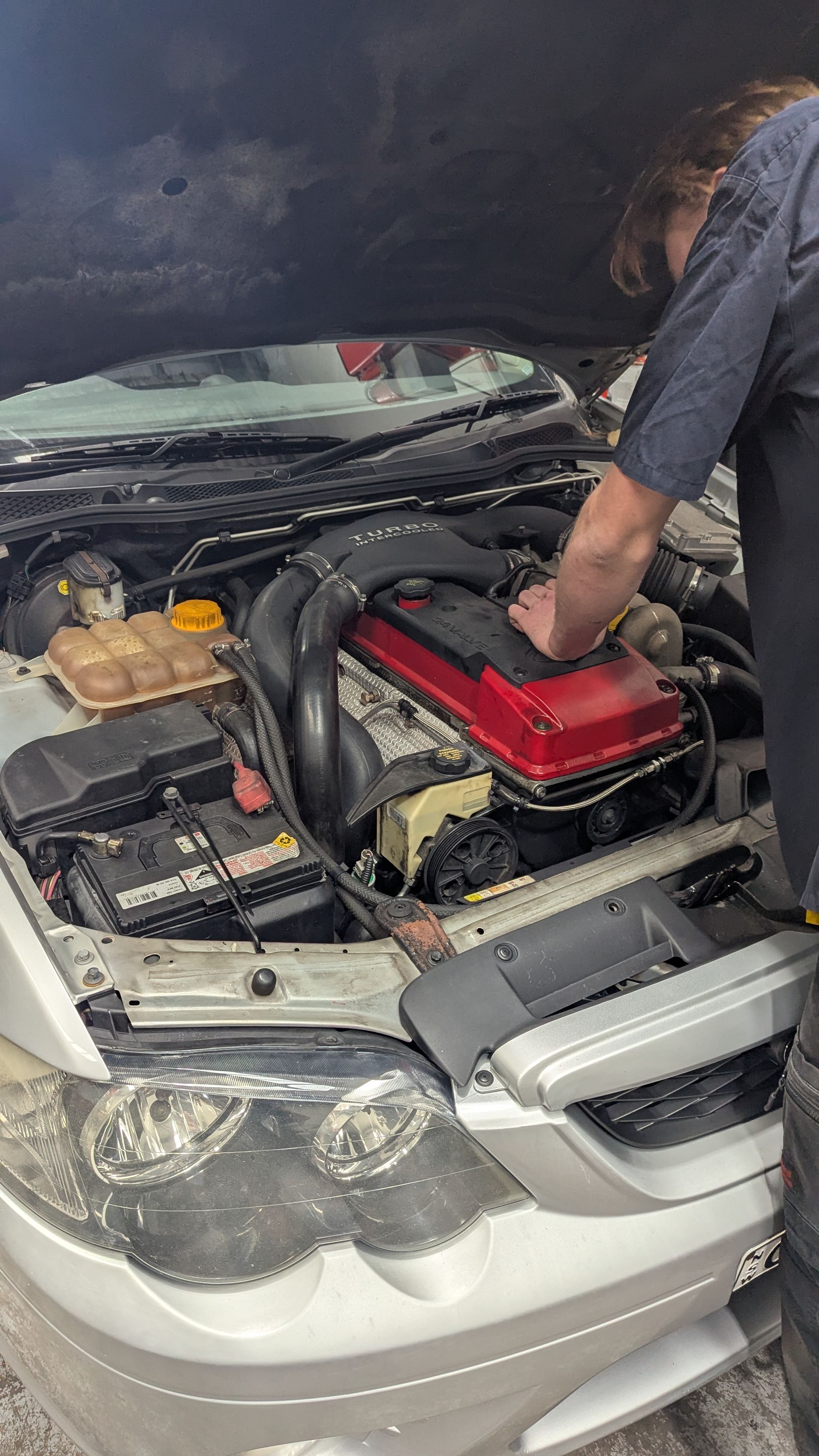 A person working on a car engine, a red cover visible, in an automotive setting  — ATD Automotive in North Wollongong, NSW