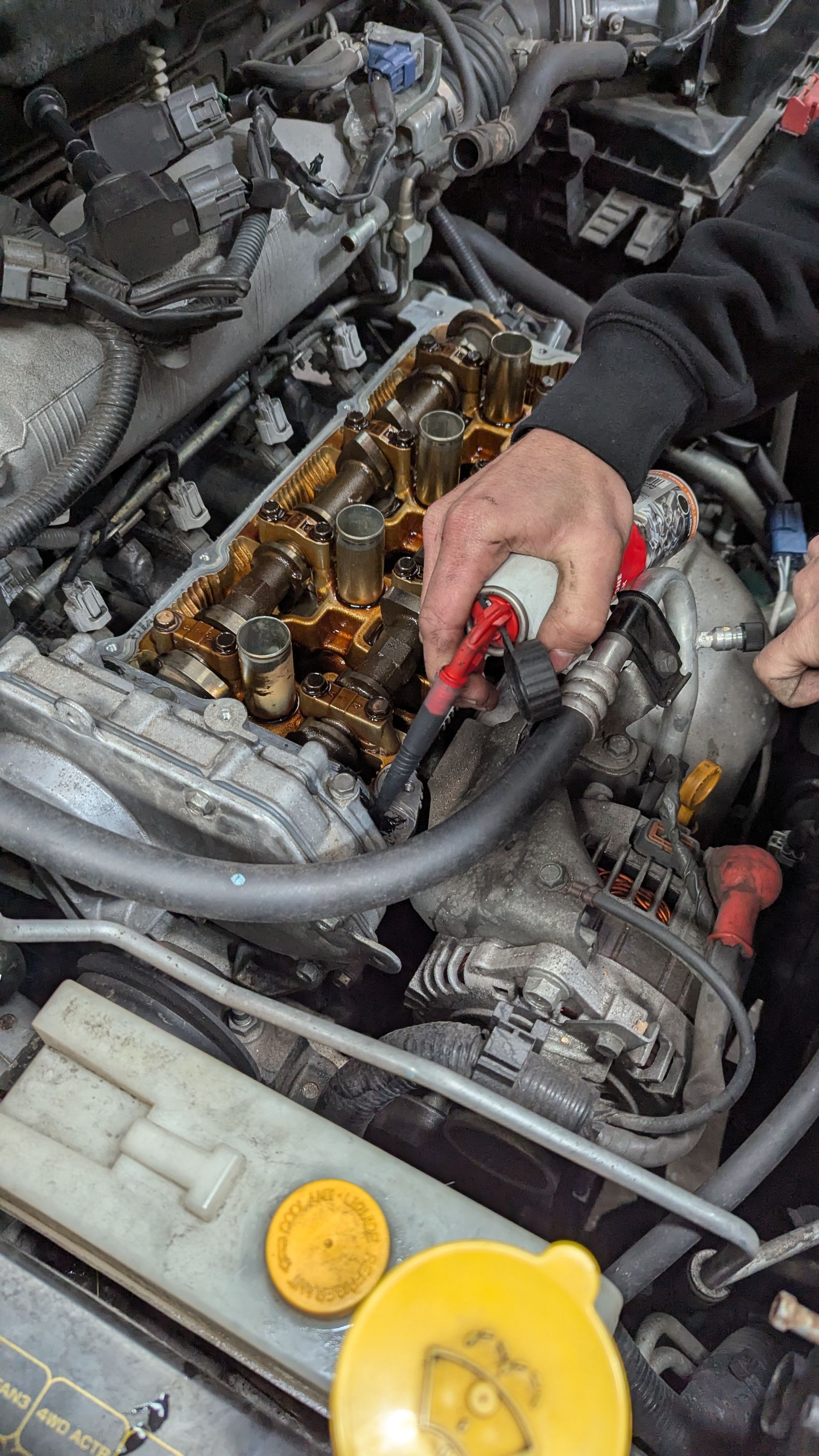 Person working on a car engine; spraying cleaner. Engine components visible. Yellow and brown tones — ATD Automotive in North Wollongong, NSW